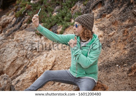 a middle-aged man with youthful style sitting on some rocks taking a picture