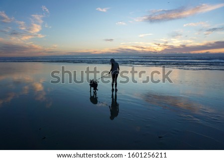 A silhouetted woman with her dog during sunset on Pacific Beach, CA.