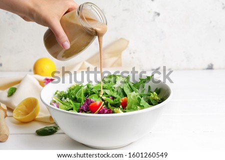 Woman pouring tasty tahini from jar onto vegetable salad in bowl Royalty-Free Stock Photo #1601260549