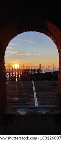 Sunrise of sea by pier under semi-circle tunnel arch