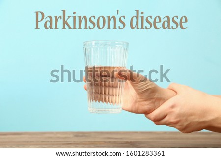 Trembling hands with glass of water and text PARKINSON'S DISEASE on color background Royalty-Free Stock Photo #1601283361