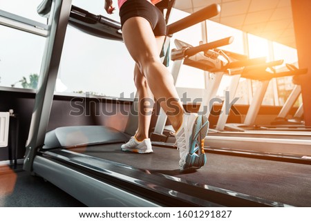 close up girls feet walking at the treadmill in the gym over sunrise. wearing in white orange blue sneakers. Cardio exercise Royalty-Free Stock Photo #1601291827