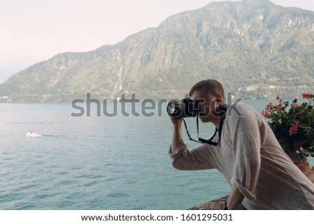 Young man takes pictures with a professional camera on a background of mountains and a lake. Photo travel concept.