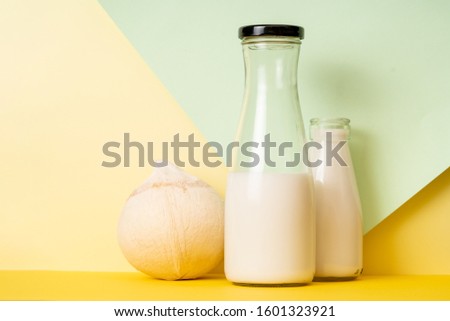 Fresh coconut fruit and glass bottled coconut milk on a solid background