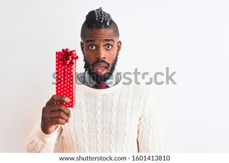 African american man with braids holding christmas gift over isolated white background scared in shock with a surprise face, afraid and excited with fear expression