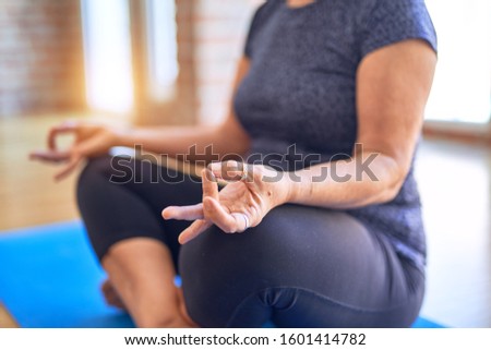 Middle age beautiful sportwoman sitting on mat practicing yoga doing lotus pose at gym