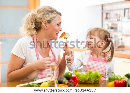 kid daughter feeding mother vegetables in kitchen