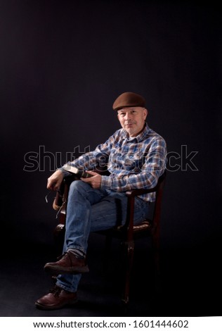 Portrait of senior man with book sitting on old chair, on black background