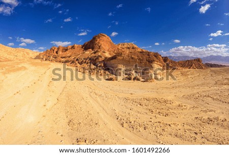 Aerial scenic panorama of rocky mountains and desert valley in Eilat region with blue cloudy sky and yellow and orange sand and stones lit with a sunset light