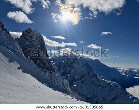 Photo in the middle of the mountains covered with snow during winter. The sun is visible and lets appear some rays between the mountains.