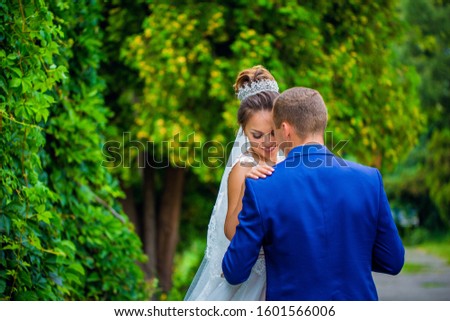 Look from behind at dreamy bride leaning to groom with wedding bouquet in her arms