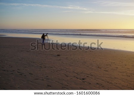 A woman stands with her tripod photographing the sunset over the Pacific Ocean.