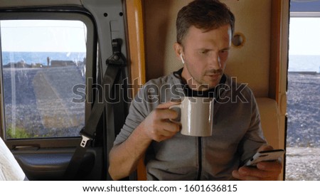 man drinks coffee and uses a smartphone sitting in a caravan by the sea. Royalty-Free Stock Photo #1601636815