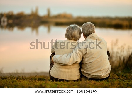 Happy senior couple sitting in summer near lake during sunset Royalty-Free Stock Photo #160164149