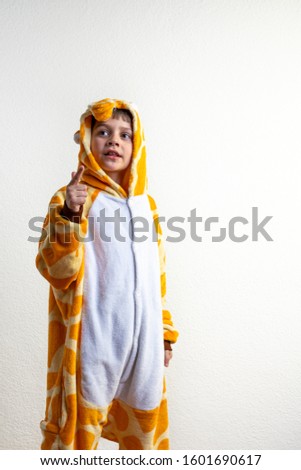 Attractive child boy dressed in giraffe pajamas standing over isolated white background, pointing with his finger up and looking at left corner, studio portrait