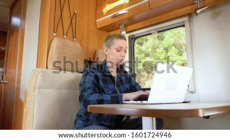 A woman uses a laptop while sitting at a table in a motor home Royalty-Free Stock Photo #1601724946