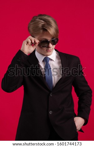 Young teenager guy in a black jacket, tie and sunglasses posing on a red background