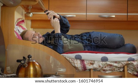 Woman uses a mobile phone lying on a bed in a motor home. Royalty-Free Stock Photo #1601746954