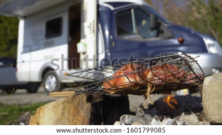 a man cooks meat on the grill outdoors on a background of motorhomes. Royalty-Free Stock Photo #1601799085