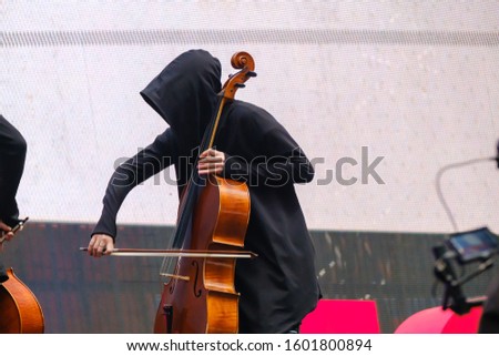 Man in a black robe with hood plays the cello