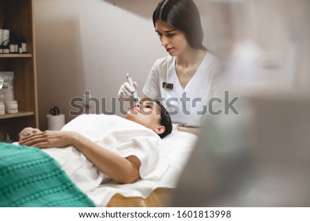 Picture of young beautician working in her cabinet. Client lying on table. Cosmetologist doing procedures. Therapy for healthy glowing look. Skincare and beauty treatment