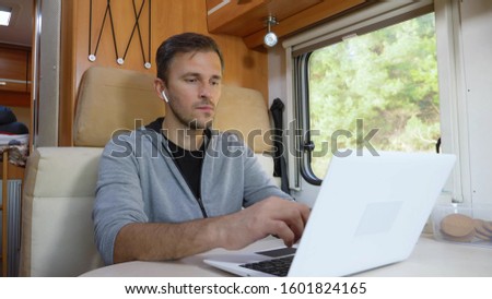 man using his laptop sitting at a table in the motorhome. Royalty-Free Stock Photo #1601824165