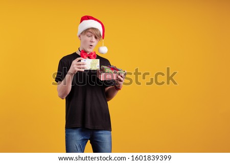 A young guy in a red Santa Claus hat holds in his hands banknotes, money and posing on a yellow background