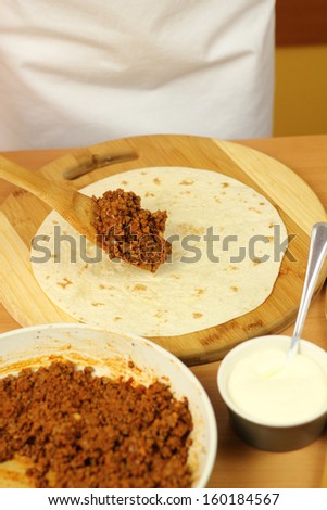 Putting portion of stuffing (ground beef) on tortillas. Making enchilada tortilla with beef. 