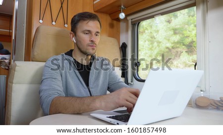 man using his laptop sitting at a table in the motorhome. Royalty-Free Stock Photo #1601857498