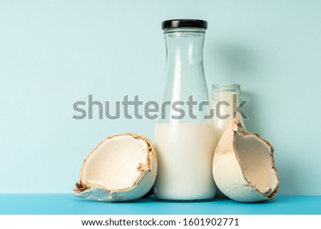 Fresh coconut fruit and glass bottled coconut milk on a solid background