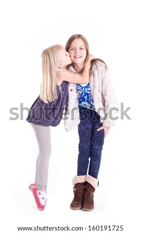 Little girl kissing her older sister. Isolated on a white background. Studio shot 