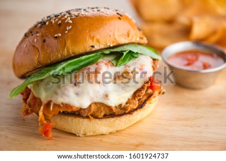 Chicken parmesan sandwich. Classic traditional chicken parmesan, breaded chicken breast battered and fried and served on sesame seed bun with melted mozzarella cheese and tomato sauce and crisp fresh Royalty-Free Stock Photo #1601924737