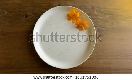 Concept picture for food and decorating. Orange Cosmos flowers decorate on white dish on brown wood background.
