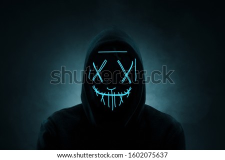 Portrait of an anonymous man, hacker wearing neon mask over dark background