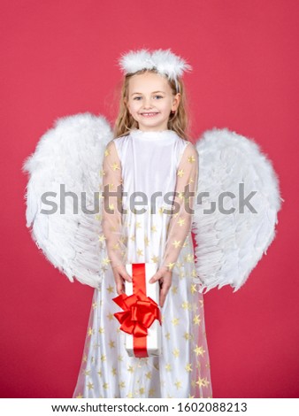 Angel child from heaven gives you gift. Cute toddler girl in white wings as Cupid. Angel kid with blonde curly hair. Happy little Angel. Wonderful blonde little girl in the image of an angel with
