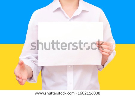 man with a white sheet of paper in his hands, for your text, mockup. Against the background of the flag of Ukraine. Unknown person. He reaches out for agreement.