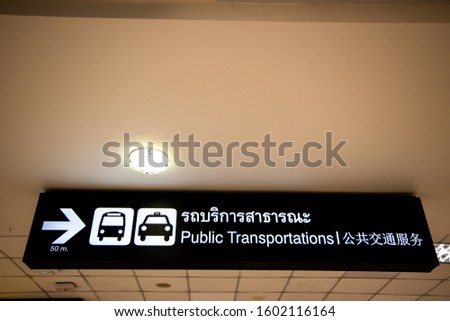 Public transportation sign in Thai, English and Chinese languages with icons of bus and taxi and arrow pointing to the right on black led panel at airport terminal.