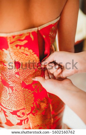 Fingers zipping a beautiful Chinese bridal dress. Oriental costume with gold pattern. China's modern wedding cloth.Asian festive season gown.  
