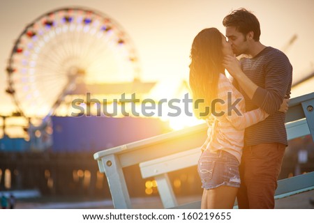 romantic couple kissing at sunset in front of santa monica ferris wheel. Royalty-Free Stock Photo #160219655