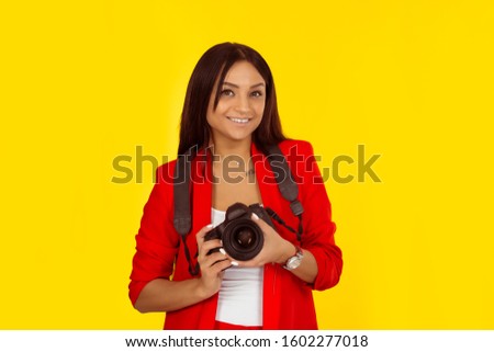 Professional female photographer holding digital camera and smiling. Mixed race model isolated on yellow background with copy space. Horizontal image. Natural, no makeup.
