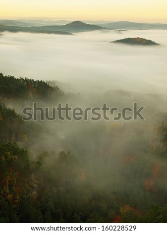 Sunrise in a beautiful mountain of Czech-Saxony Switzerland. Sandstone peaks and hills increased from foggy background, the fog is orange due to sun rays. 