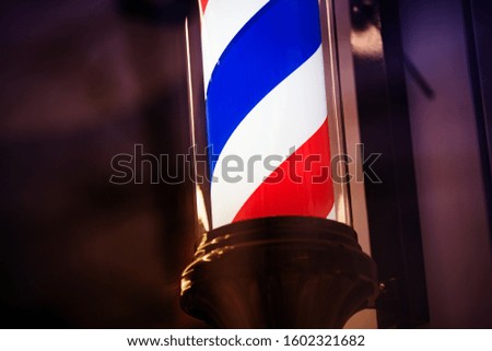 A Barber shop sign with dark caps. The background is blurred. The tricolor scrolls in the form of a spiral.