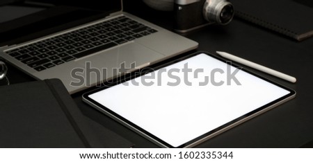 Close-up view of dark luxury workplace with open blank screen laptop computer and office supplies 