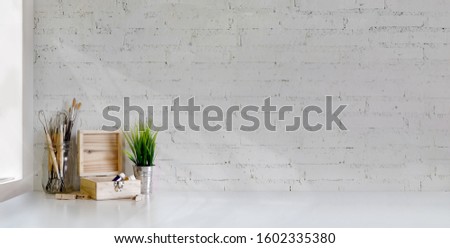 Cropped shot of minimal artist workplace with painting tools on white table and white brick wall background 