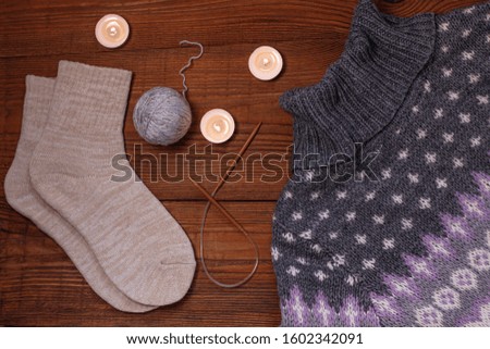 Cozy flatlay. Knitted socks, ornament sweater, candles, knitting needles, yarn on wooden background flat lay.Winter holidays concept. Weekend at home. Trendy knitted clothes, top view. Fashion design.