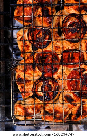 grilling spiced chicken in grid on charcoal bbq with tomatoes and vegetables