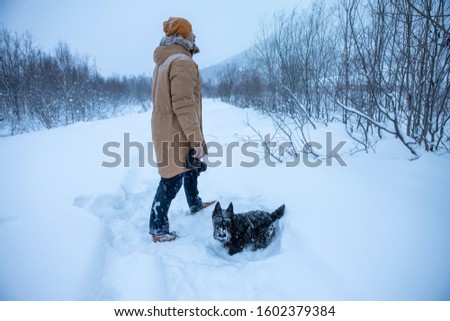 A man photographs his dog on winter walk in the snow.