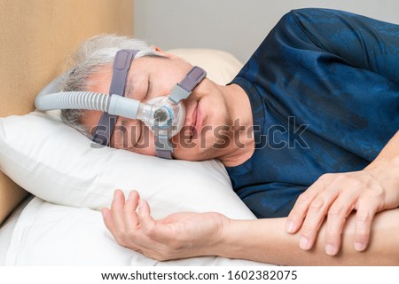 Middle age Asian man wearing CPAP headgear during his sleep Royalty-Free Stock Photo #1602382075