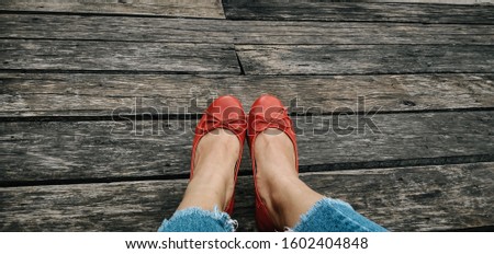 Photo of female legs wearing ripped jeans and red shoes on the old wooden background.