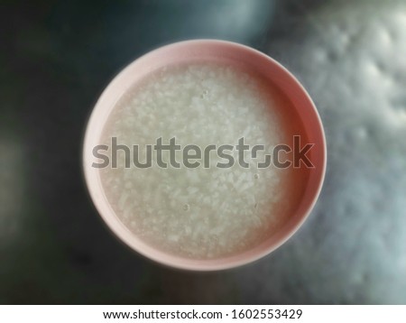 Top view image of hot boiled rice in a pink melamine bowl on a metal table, shot with blurred background and light shadow.